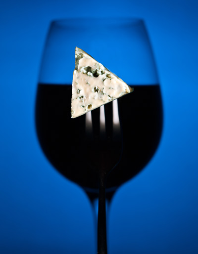 Piece of Stilton in the shape of a Play icon, on a folk, in front a glass of Port.